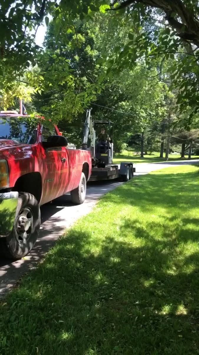 Red pickup towing compact landscape equipment on a trailer